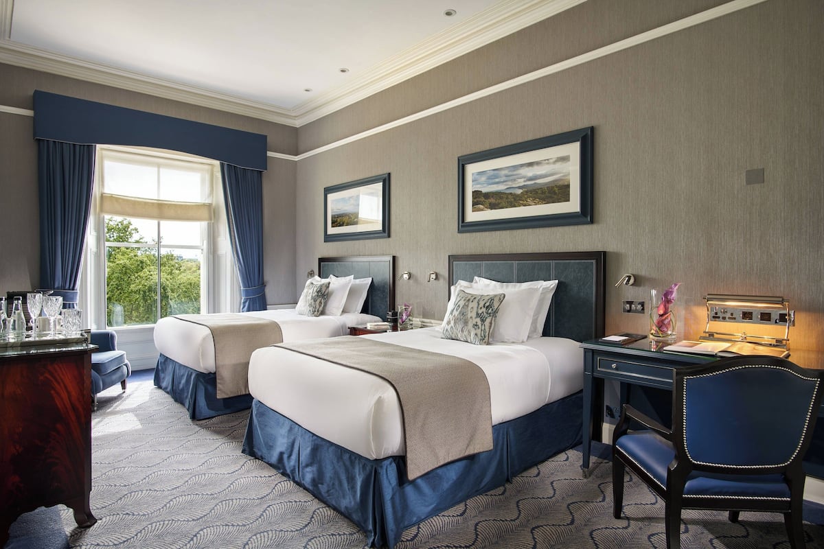 Habitación de hotel con dos camas, un escritorio, una silla y vistas al exterior.
