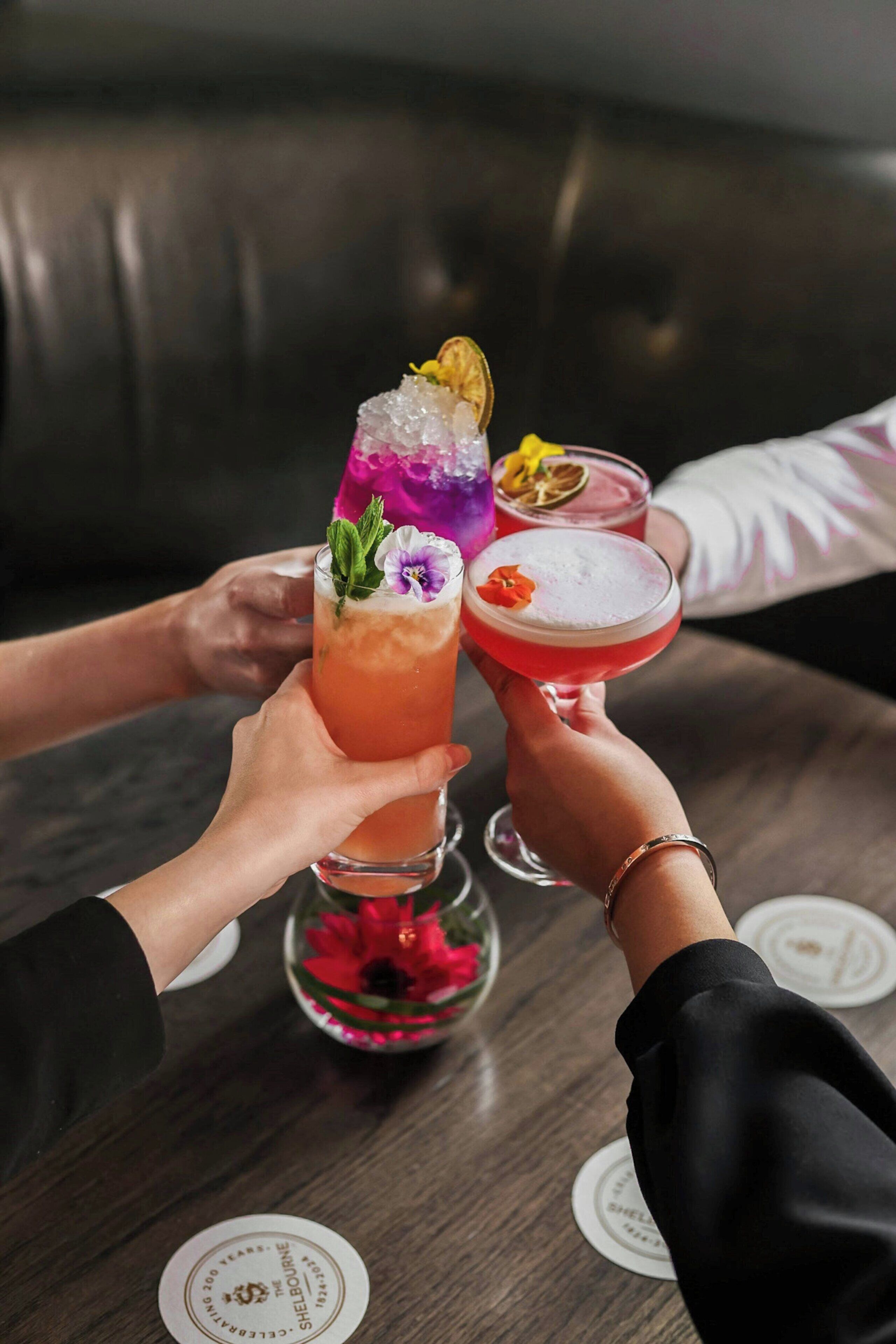 A group of people holding cocktail glasses with various garnishes on a wooden table.