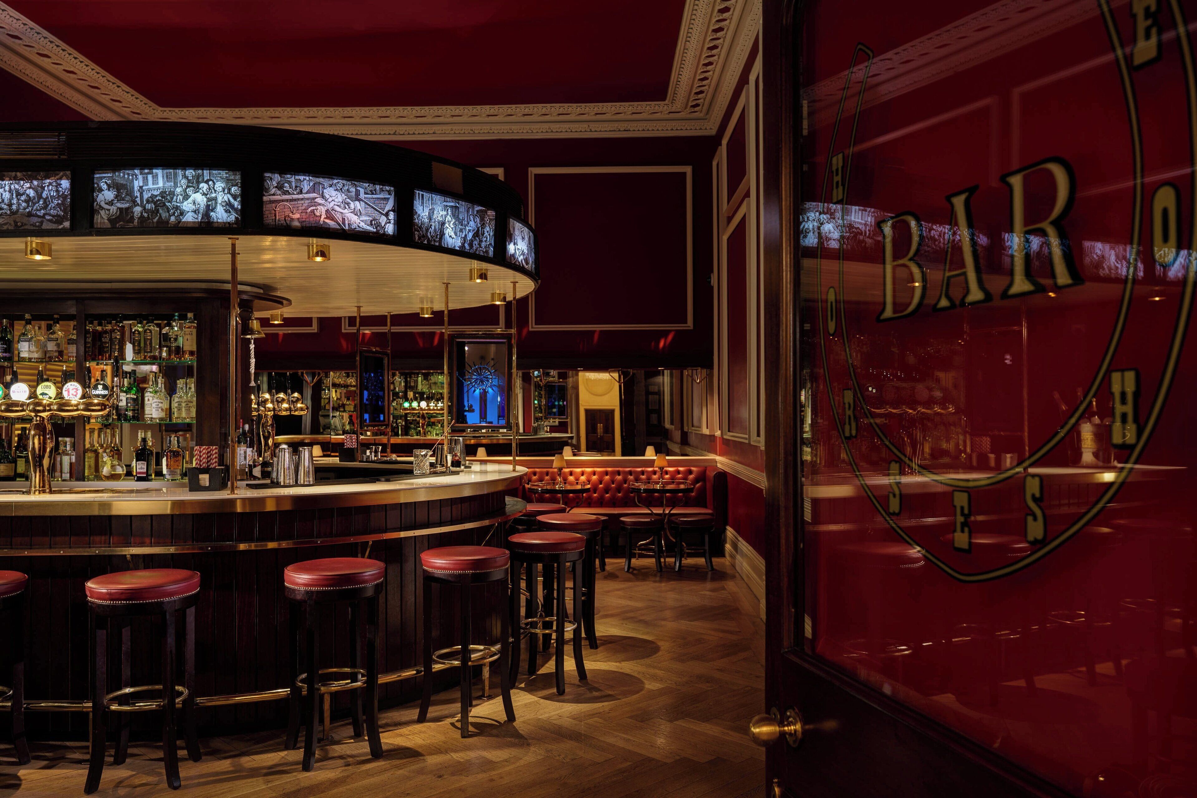 A bar area with a curved counter, multiple stools, and a seating area with red upholstered chairs.