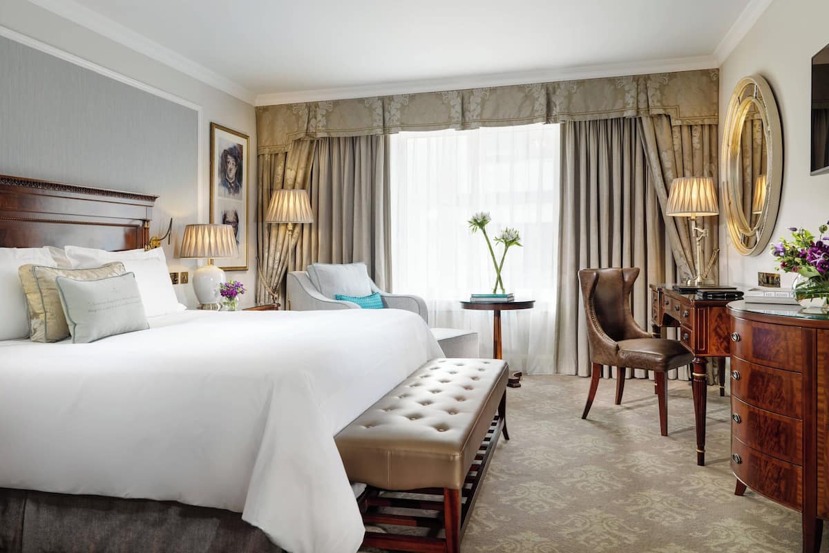 Habitación de hotel con una cama grande, un banco, un escritorio, una silla y un espejo.