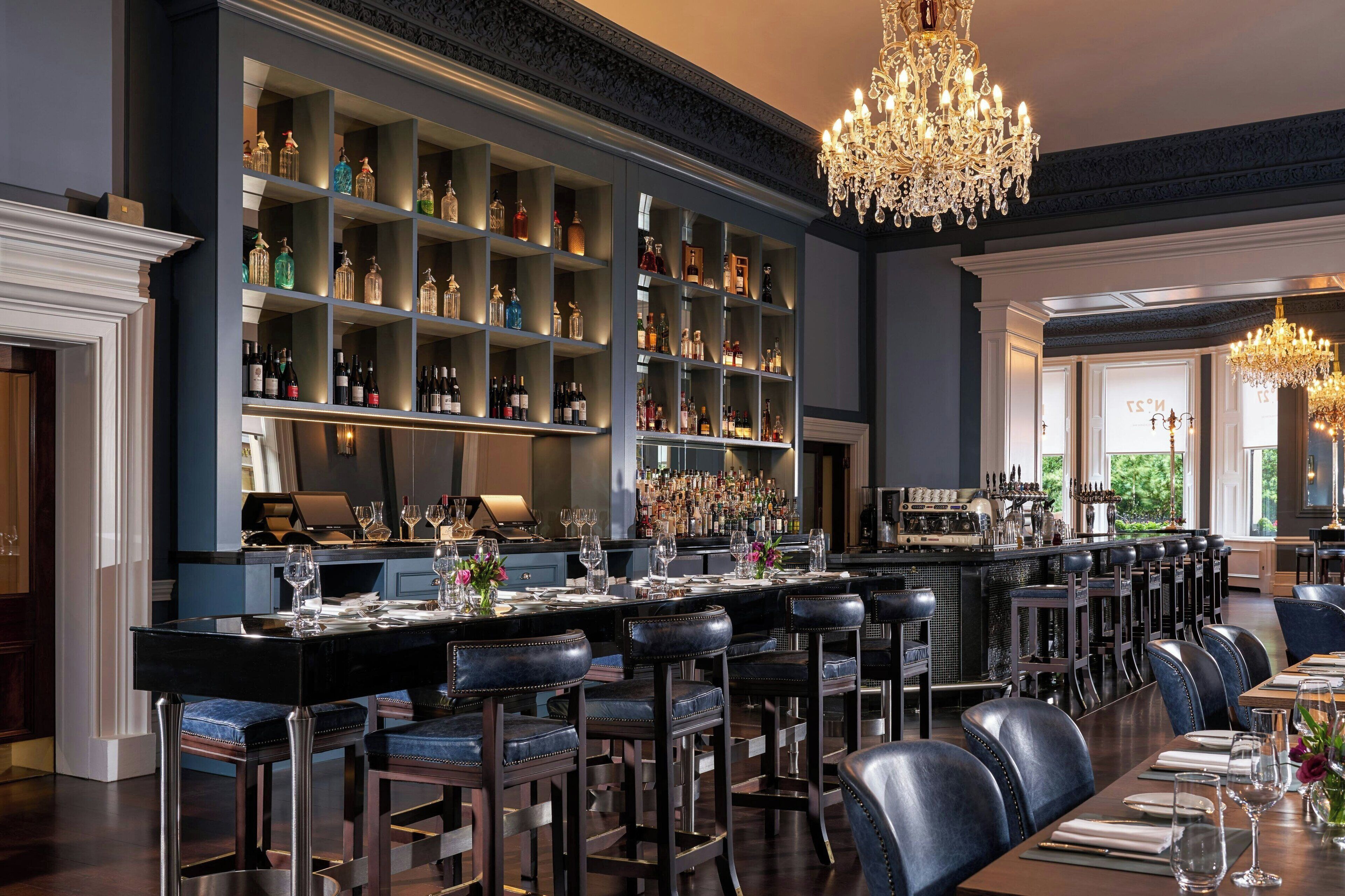 A bar area with a long counter, multiple stools, and a well-stocked liquor shelf.