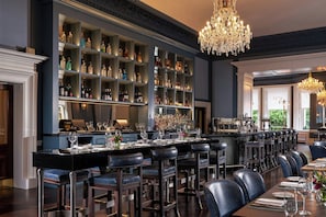 A bar area with a long counter, multiple stools, and a well-stocked liquor shelf.