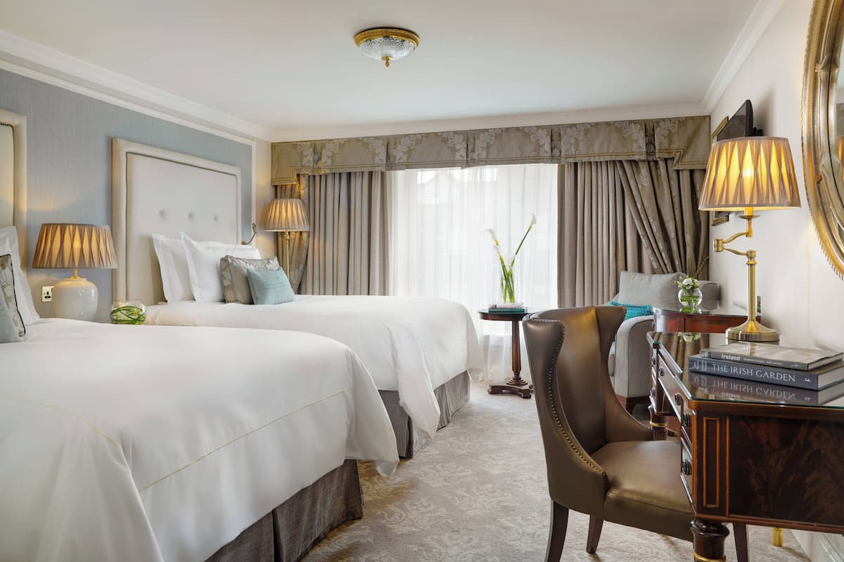 Habitación de hotel con dos camas, un área de descanso con una silla, una mesita y una lámpara.