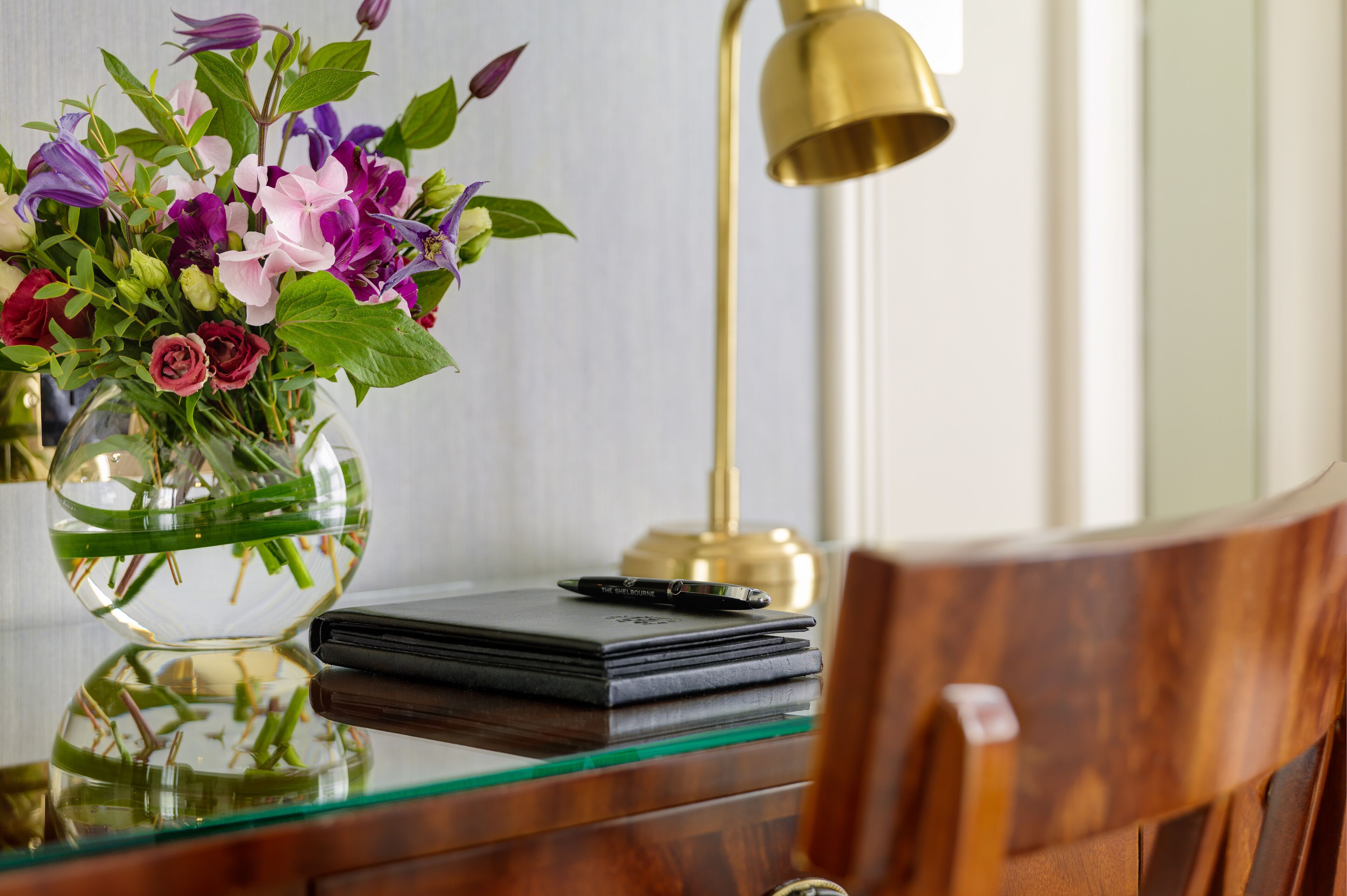A desk with a vase of flowers, a lamp, and a notebook.