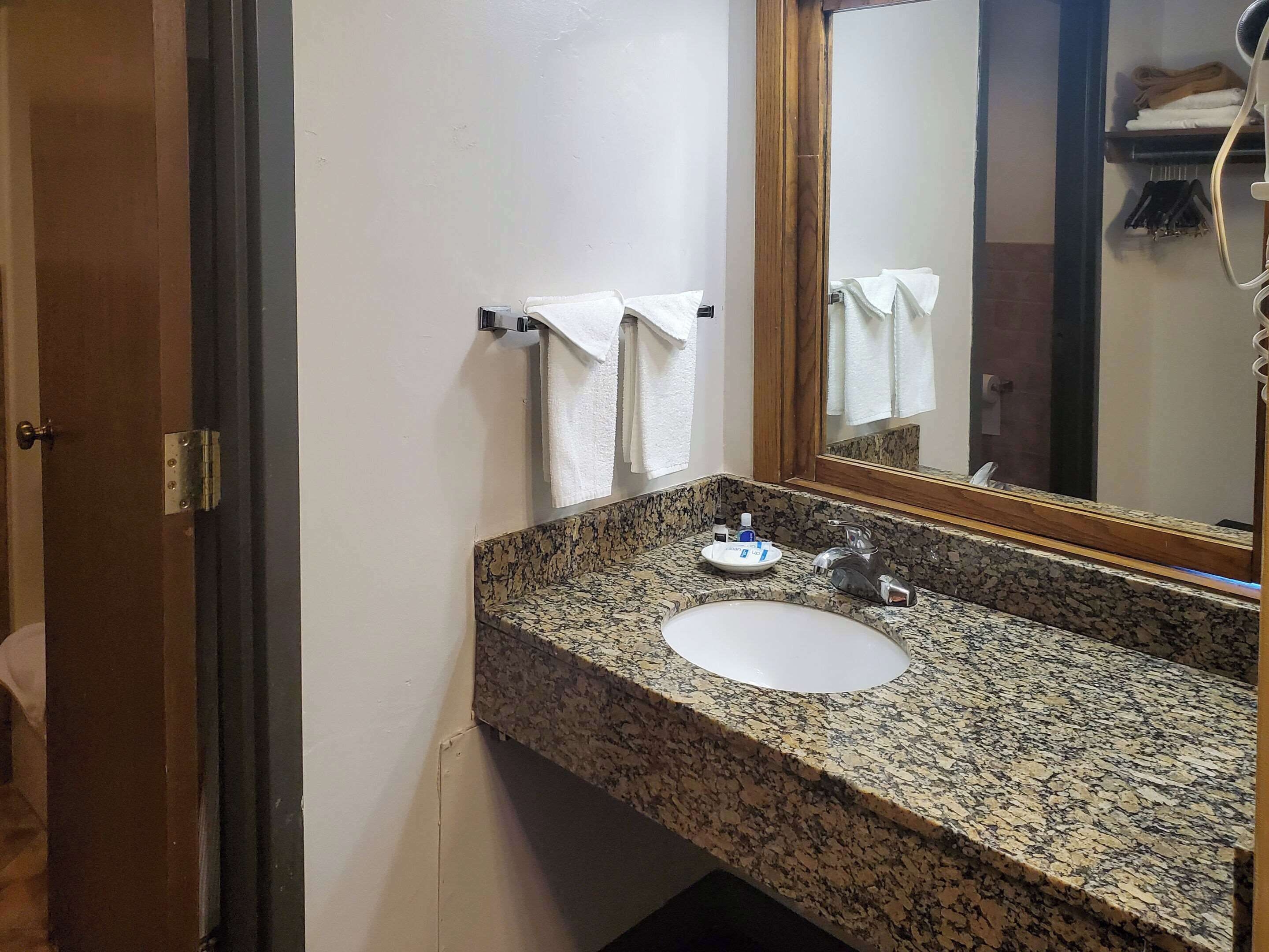 Un baño con encimera de granito, un lavamanos, un espejo y un perchero para toallas.