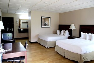 A hotel room with two beds, a desk with a chair, a desk lamp, a coffee maker, and a framed picture on the wall.