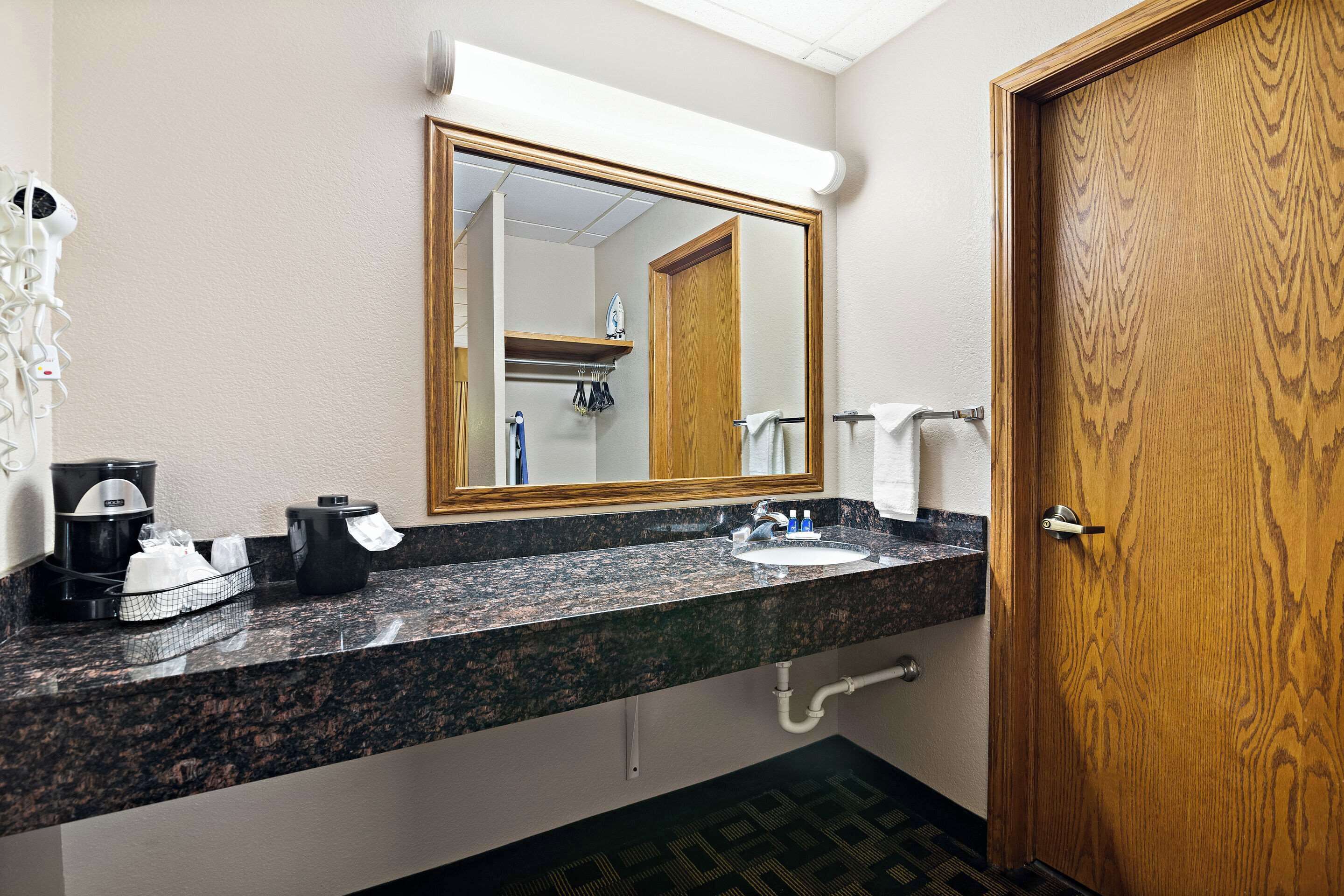 A hotel bathroom with a granite countertop, a sink, a mirror, a wooden door, and a towel rack.