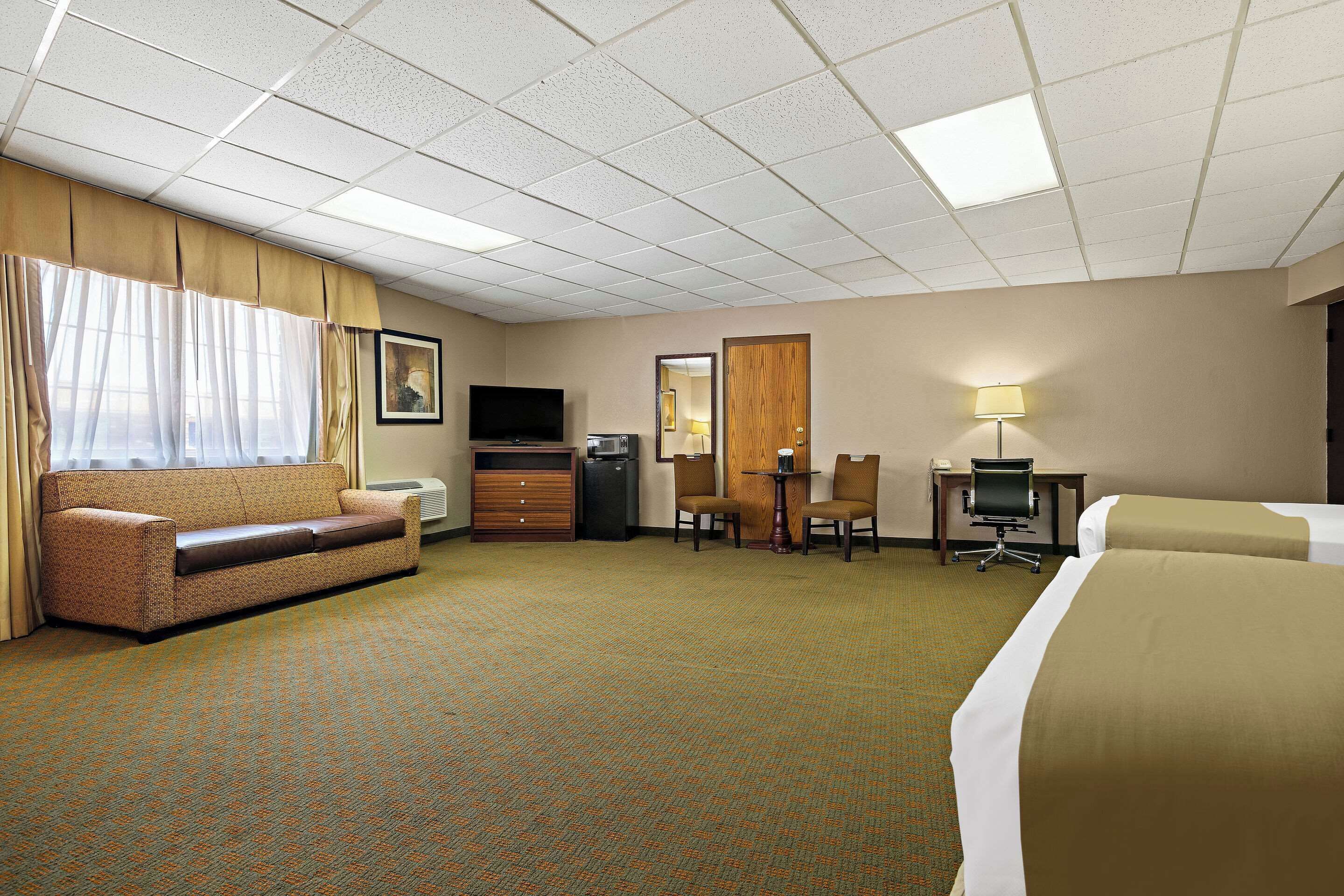 Quarto de hotel com cama, sofá, escrivaninha, cadeira, televisão e abajur.