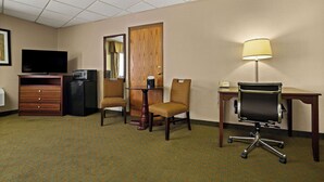 Une chambre d’hôtel équipée d’une télévision, d’un bureau avec une lampe, d’une chaise, d’une commode et d’un miroir.