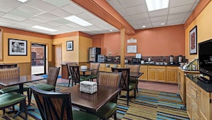 Une salle à manger d’hôtel avec plusieurs tables et chaises, un coin cuisine et un téléviseur.