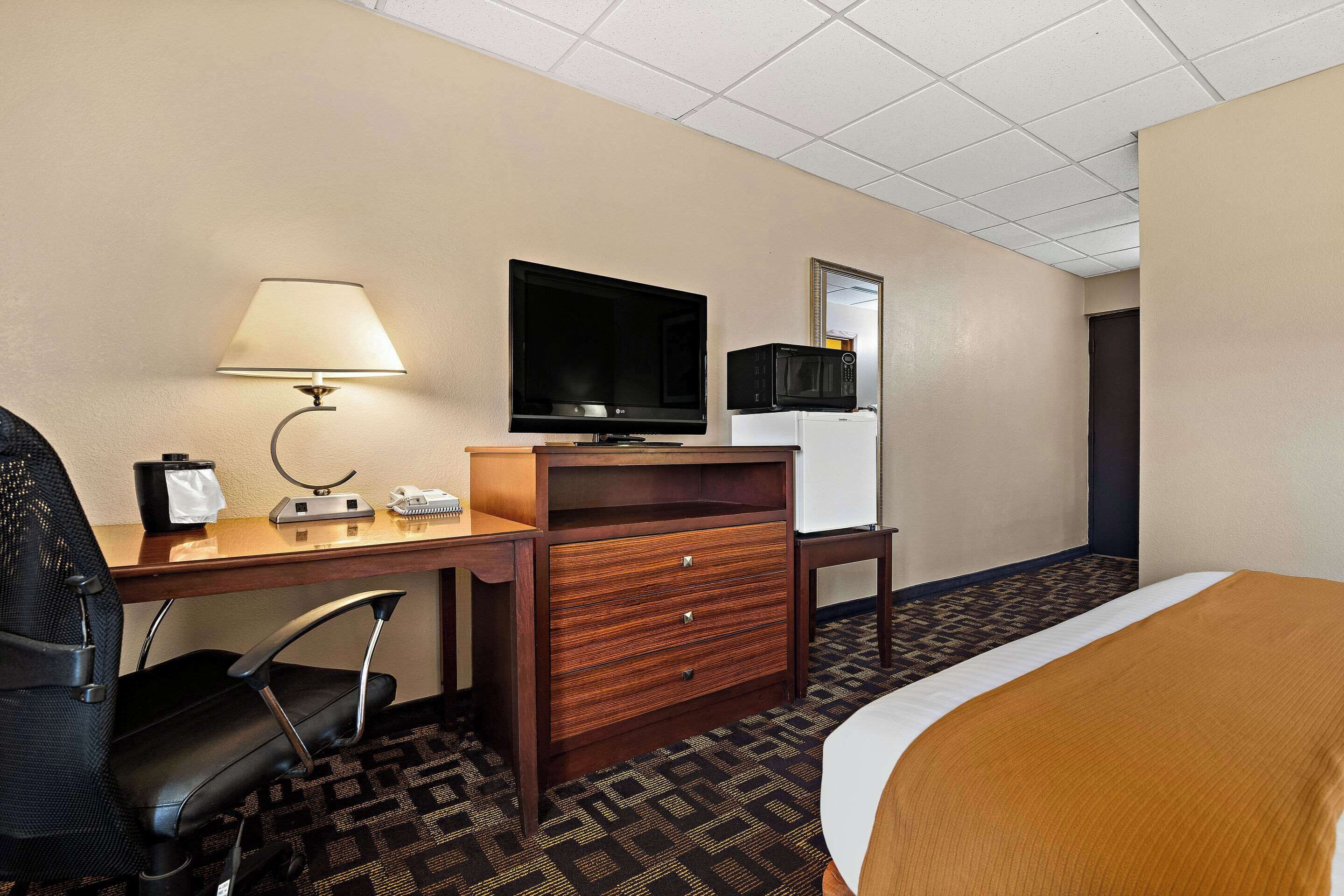 Een hotelkamer met een bed, een bureau met een lamp, een televisie, een magnetron en een stoel.
