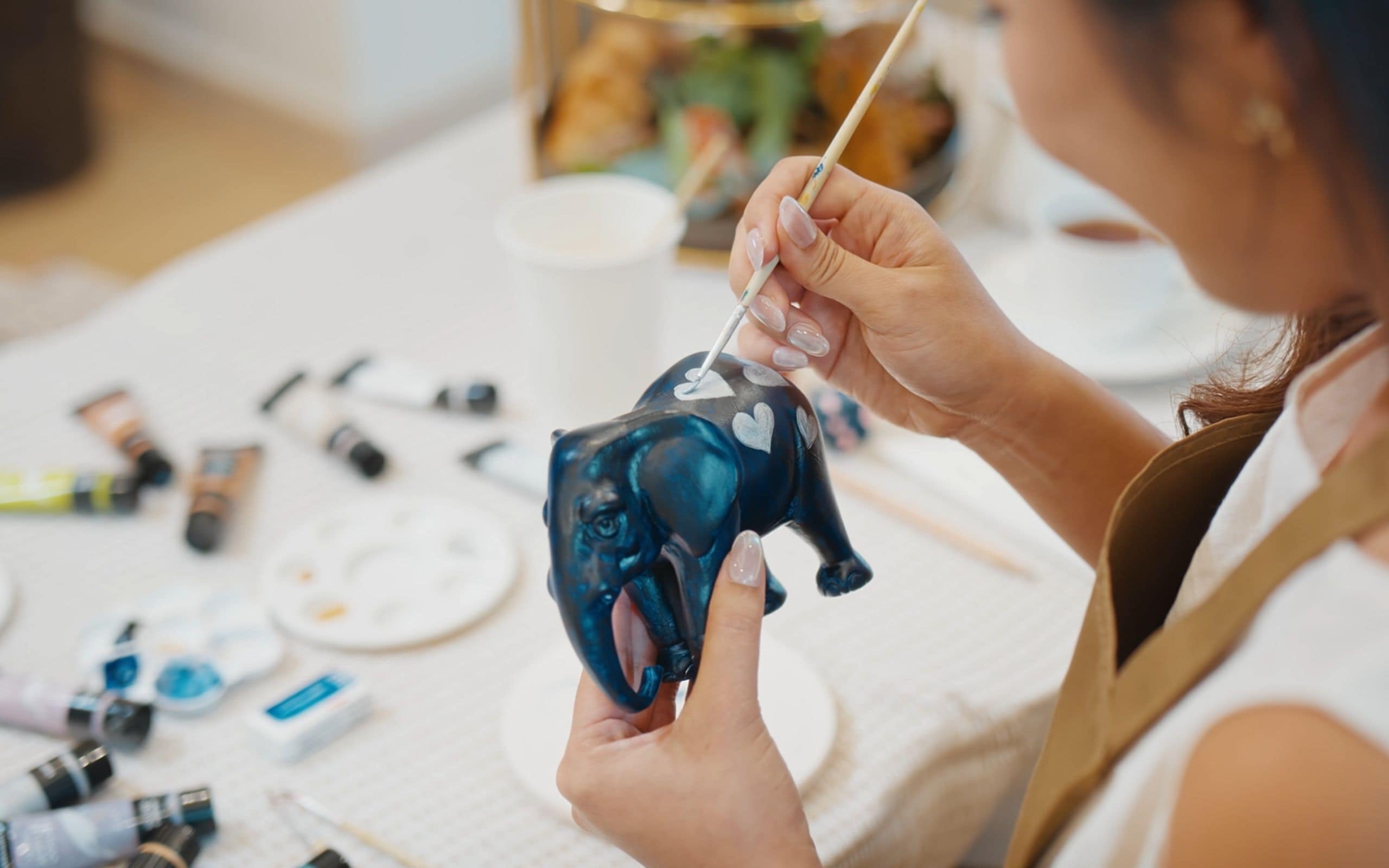 Une personne peignant une figurine d’éléphant bleue à l’aide d’un pinceau.