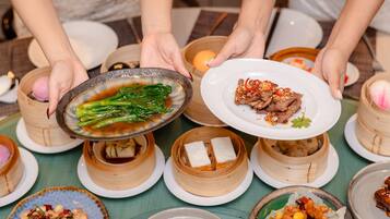 A table with various dishes, including a plate with meat and vegetables, a bowl with greens, and several bamboo steamers.