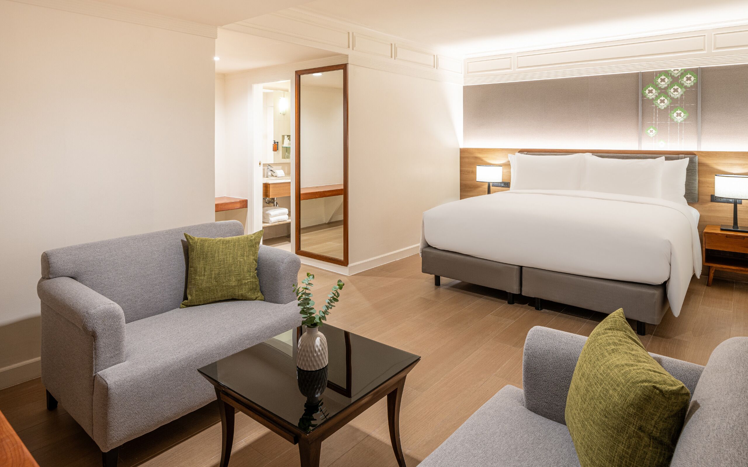 Habitación de hotel con cama, dos sillones, una mesita de centro y un baño visible a través de una puerta abierta.