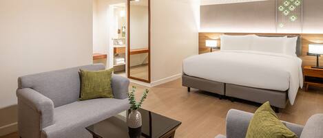 Habitación de hotel con cama, dos sillones, una mesita de centro y un baño visible a través de una puerta abierta.