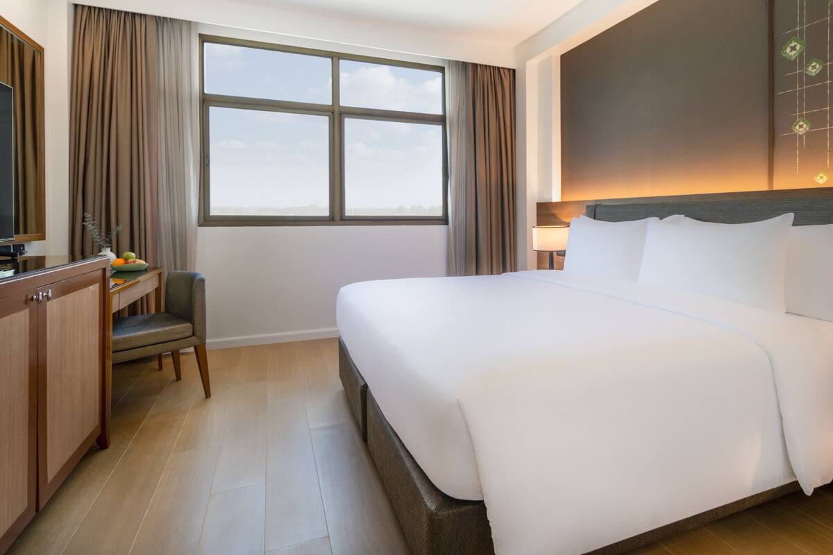 Ein Hotelzimmer mit einem großen Bett, einem Schreibtisch mit Stuhl, einem Fernseher und einem Fenster mit Vorhängen.