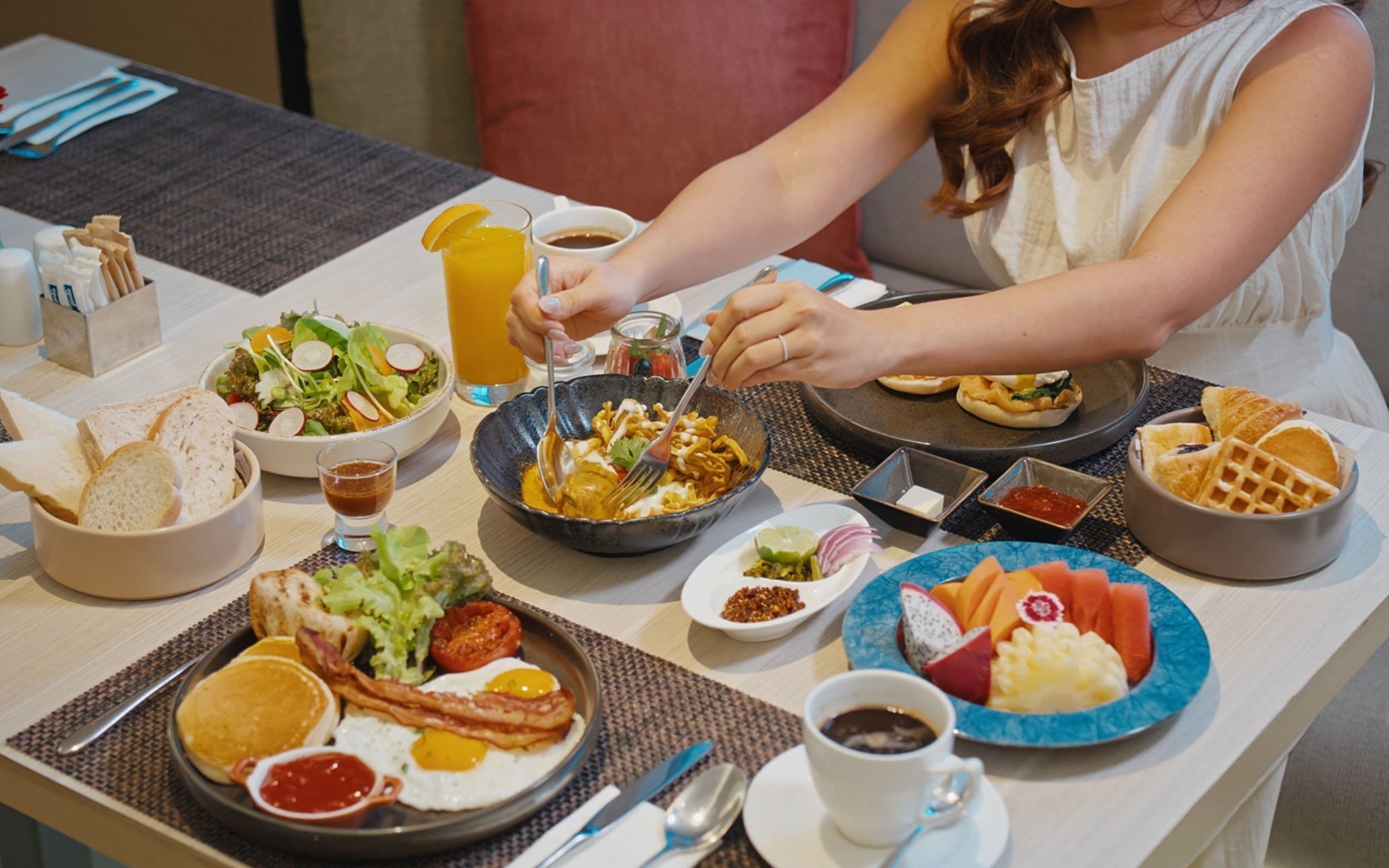 Une table dressée pour le petit-déjeuner, avec différents plats, notamment des œufs, du bacon, des toasts et des fruits.