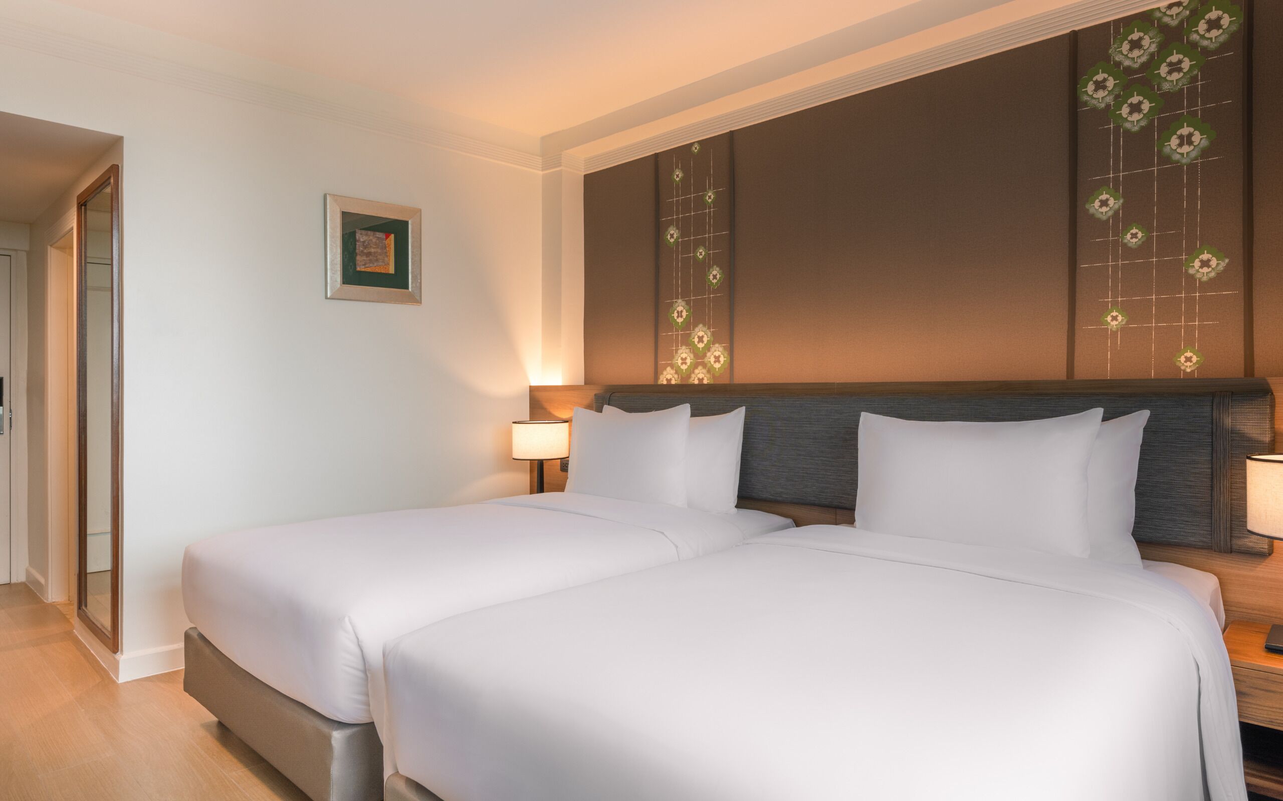 A hotel room with two beds, a wooden headboard, a wall-mounted lamp, and a framed picture.