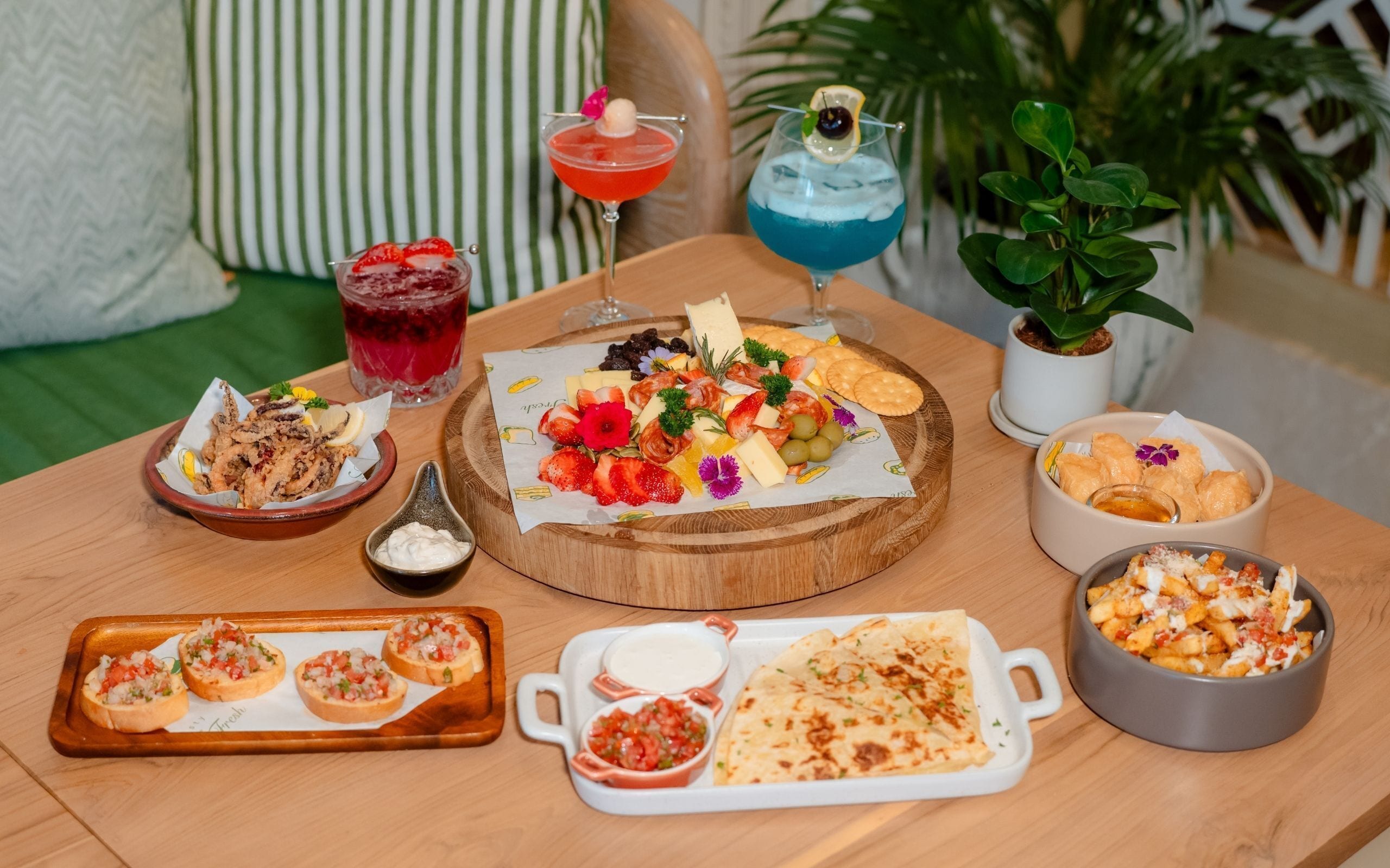 A variety of food items on a wooden table, including appetizers, a charcuterie board, and drinks.