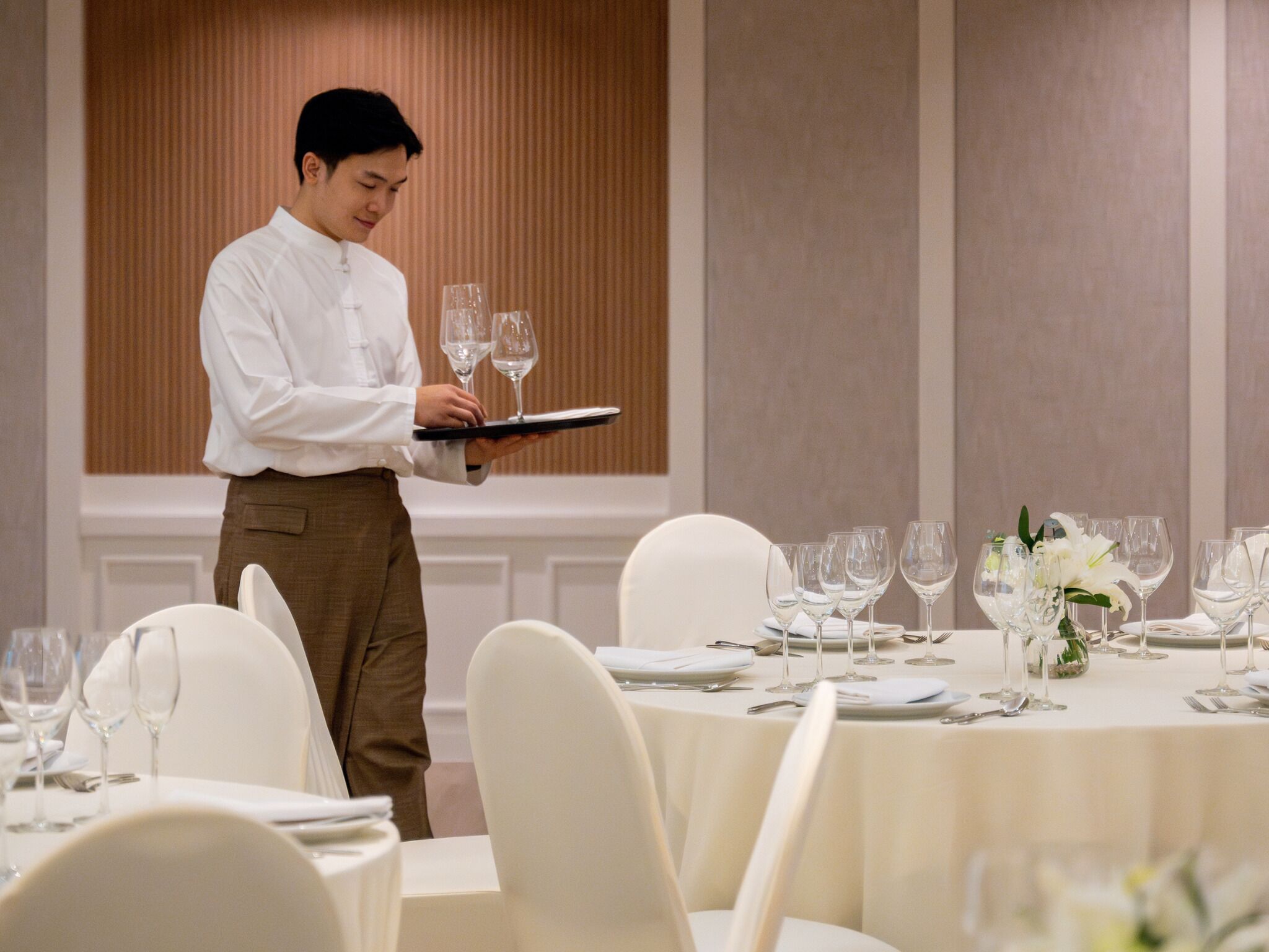 A waiter carrying a tray with glasses, standing in front of a table set for a formal dining experience.