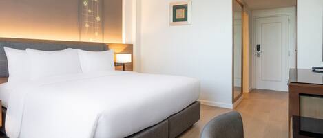 A hotel room with a large bed, a desk, and a mirror.