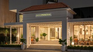 Ett hotell som heter ”DUSITPRINCESS” med en överbyggd entré, en utesittplats och krukväxter.