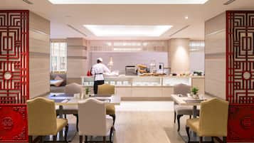 A modern dining area with a chef preparing food at a counter, wooden flooring, and traditional red decor elements.