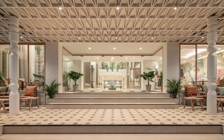 A hotel lobby with a geometric ceiling design, a central reception desk, and a seating area with chairs and tables.