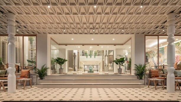 En hotelllobby med ett geometriskt utformat tak, en central receptionsdisk och en sittgrupp med stolar och bord.