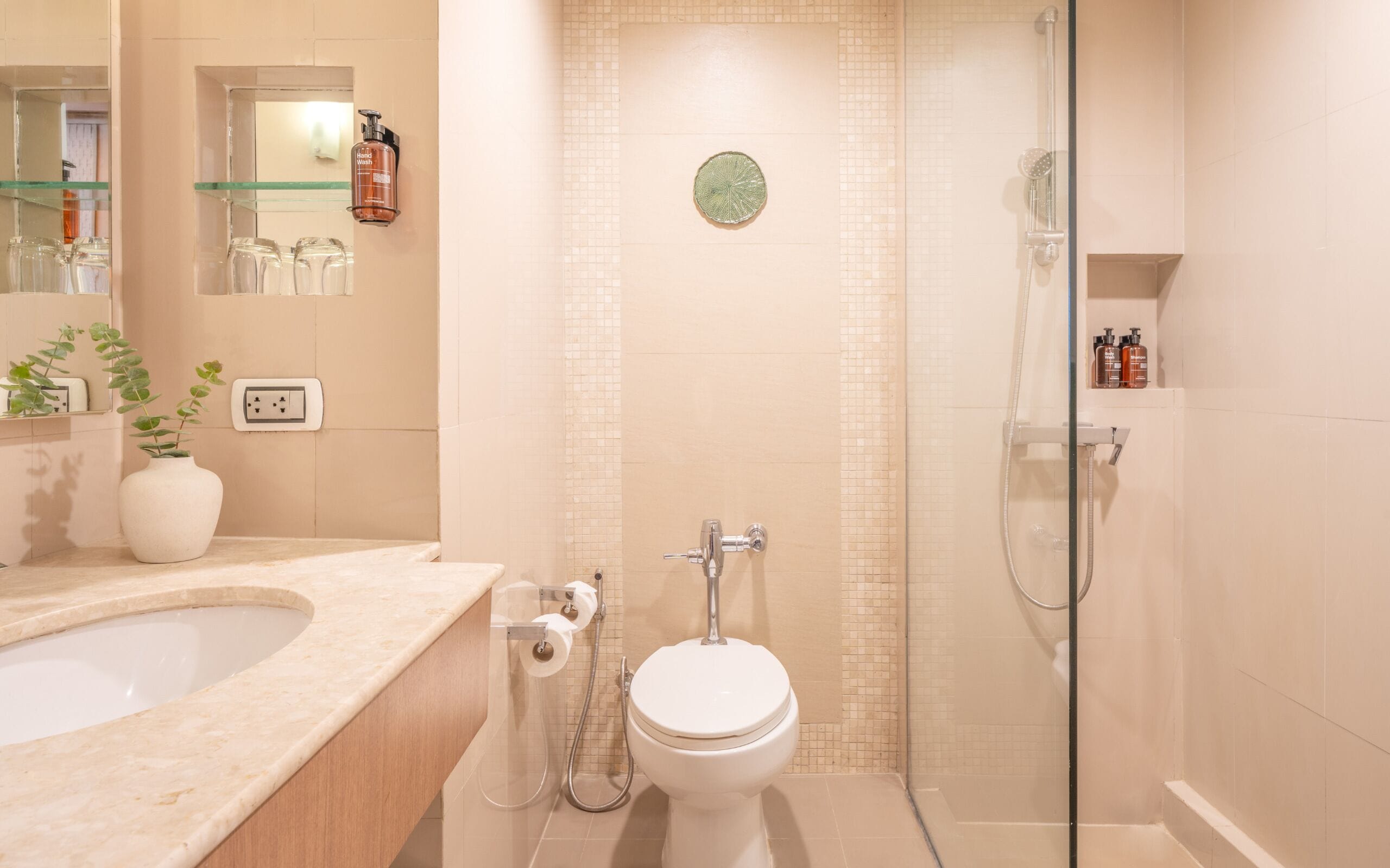 A modern bathroom with a glass-enclosed shower, a white toilet, and a beige tiled wall.