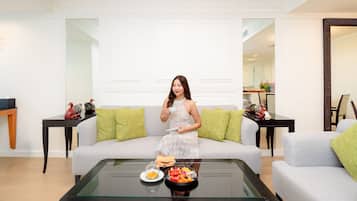 Una mujer sentada en un sofá gris en un salón luminoso, con una mesa de centro de cristal frente a ella.