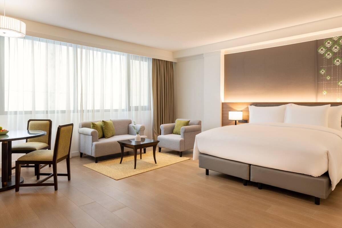 Ein Hotelzimmer mit einem großen Bett, zwei Sesseln, einem kleinen Tisch und einem Essbereich mit Stühlen und einem Tisch.