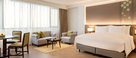 A hotel room with a large bed, two armchairs, a small table, and a dining area with chairs and a table.