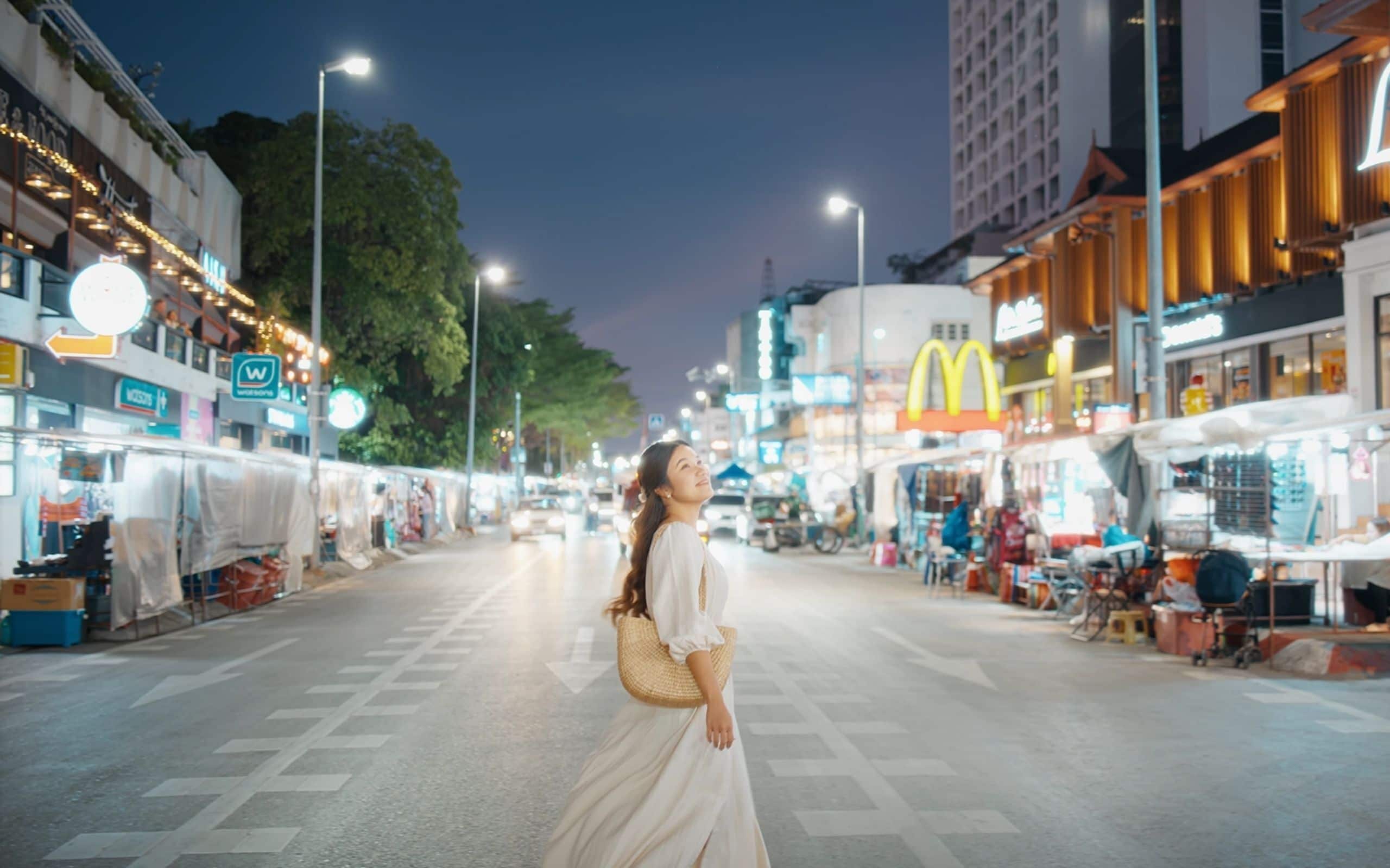 A nighttime street scene with a pedestrian crossing and various commercial establishments, including a McDonald's.
