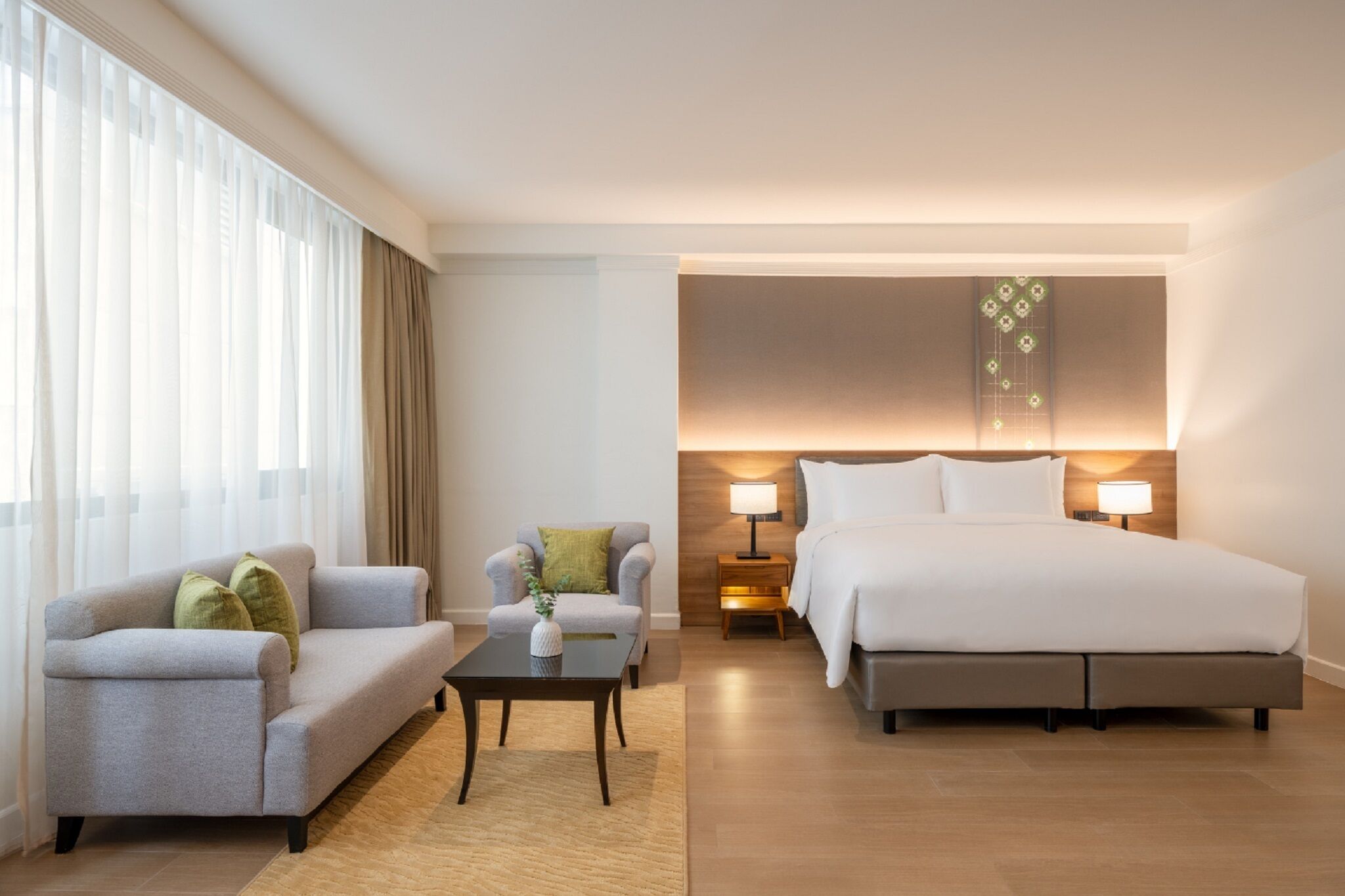 Une chambre d’hôtel avec un lit, un canapé, une petite table et une table de chevet avec des lampes.
