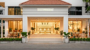 Entrada de un hotel con un letrero que dice "DUSITPRINCESS", que presenta un espacio al aire libre acogedor con plantas en macetas y un interior bien iluminado.