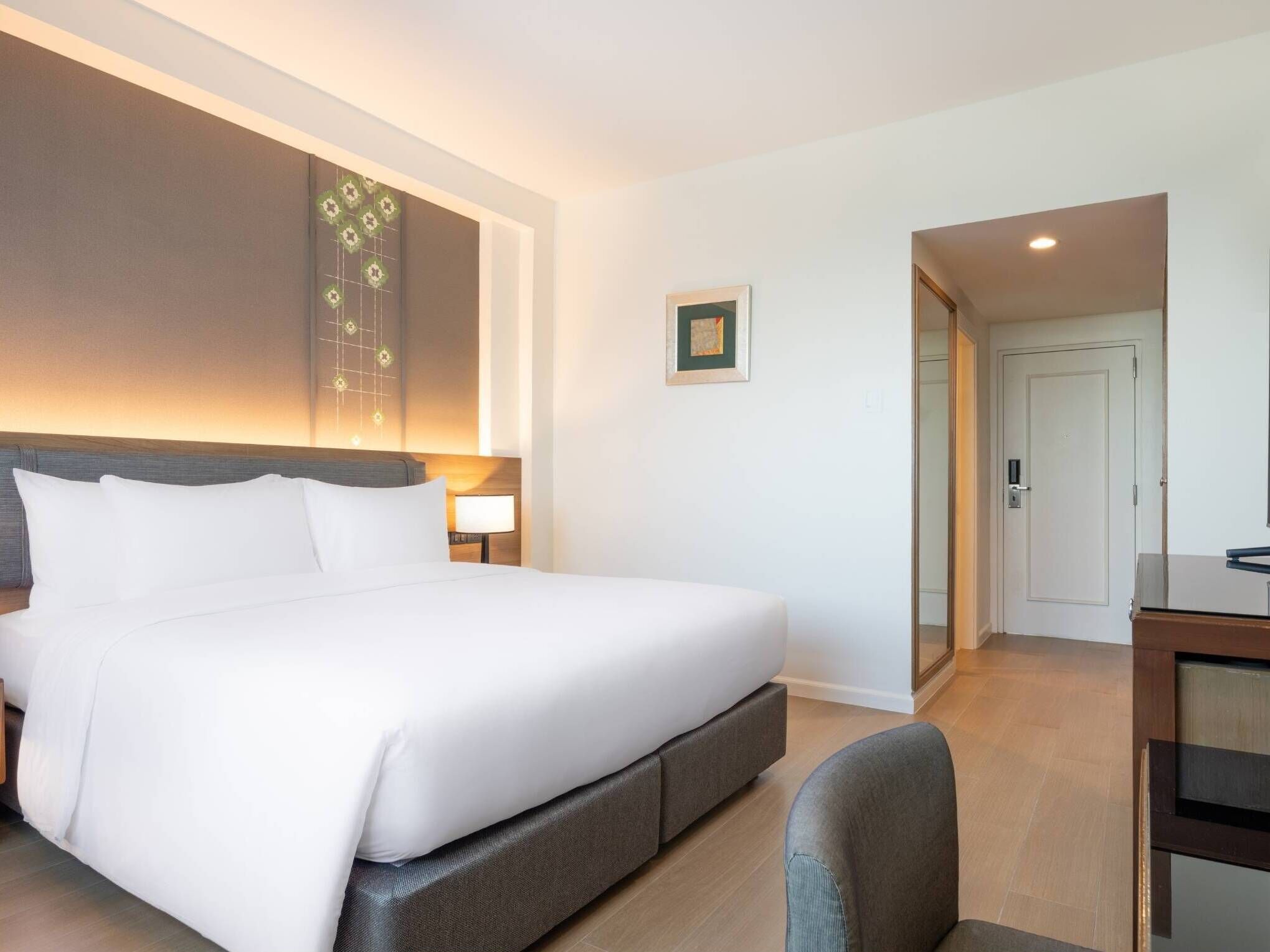 Une chambre d’hôtel avec un grand lit, une table de chevet avec une lampe, un petit tableau encadré au mur et une porte donnant sur une salle de bain.