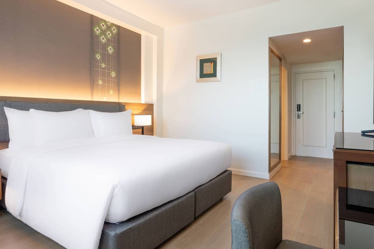 A hotel room with a large bed, a bedside table with a lamp, a small framed picture on the wall, and a door leading to a bathroom.