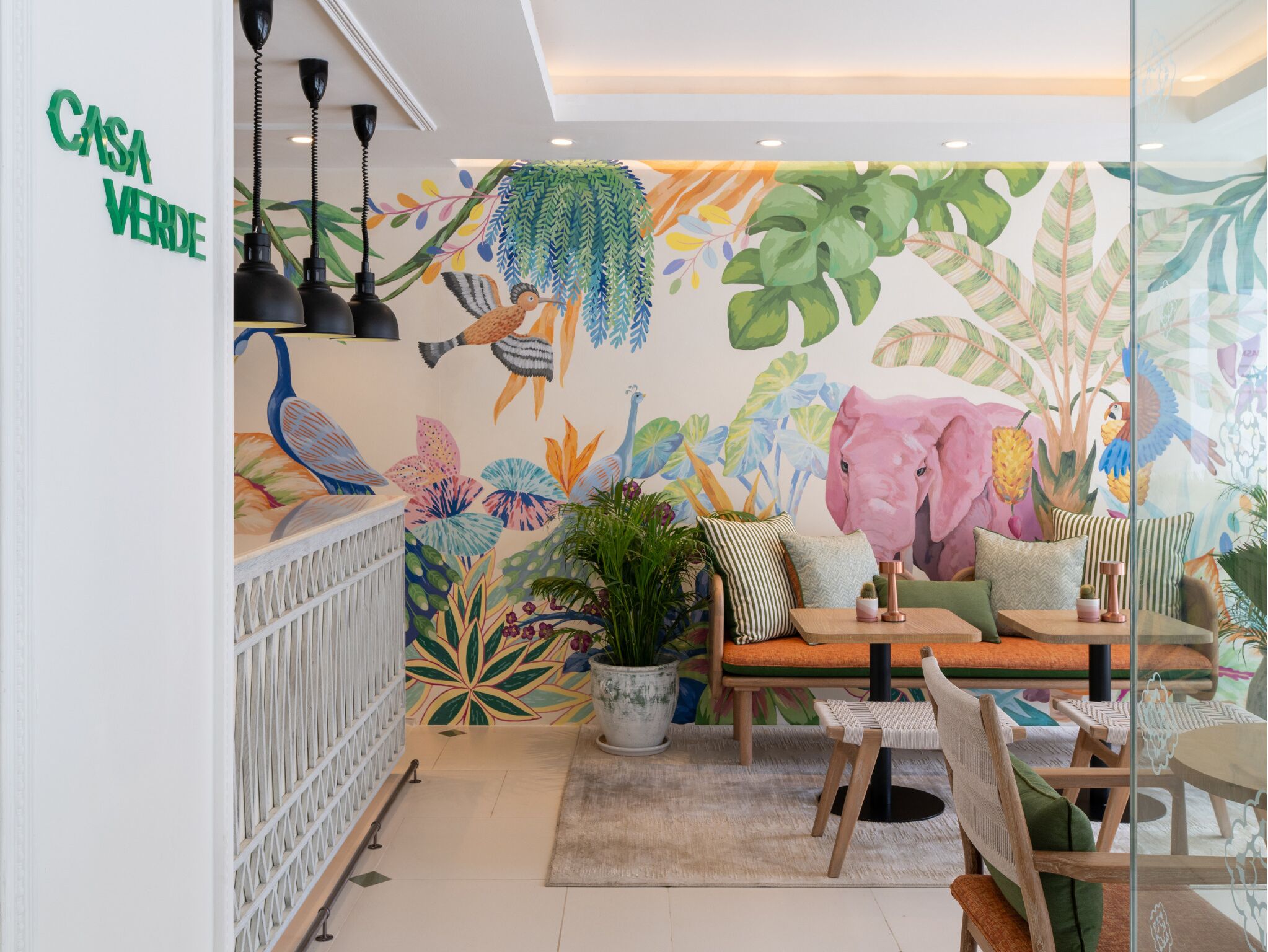 Un espacio interior acogedor con un mural llamativo, una zona de estar con mesa y sillas, y una planta en maceta.