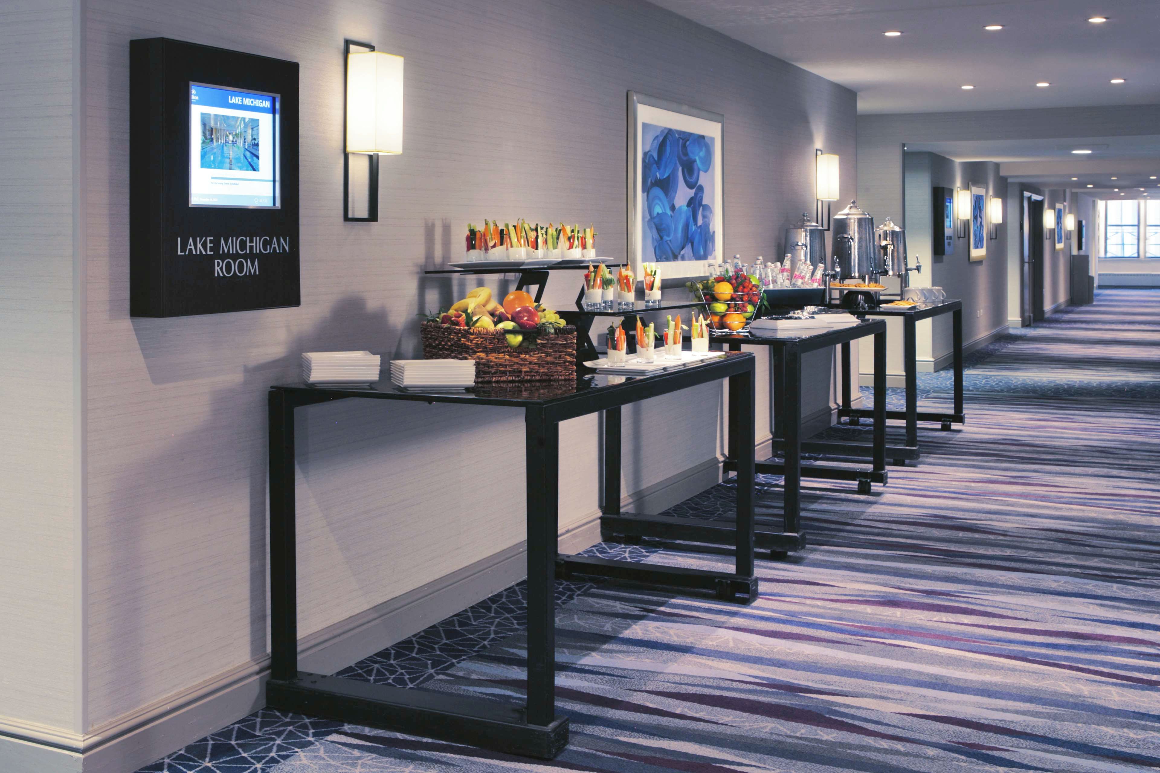Un couloir d’hôtel où est installé un buffet proposant des fruits, des légumes et des boissons.