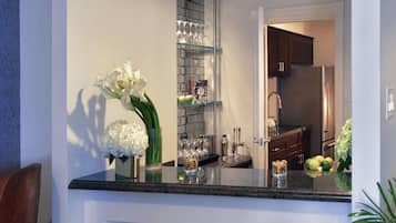 A kitchen with a marble countertop, a refrigerator, and a glass shelf with kitchenware.