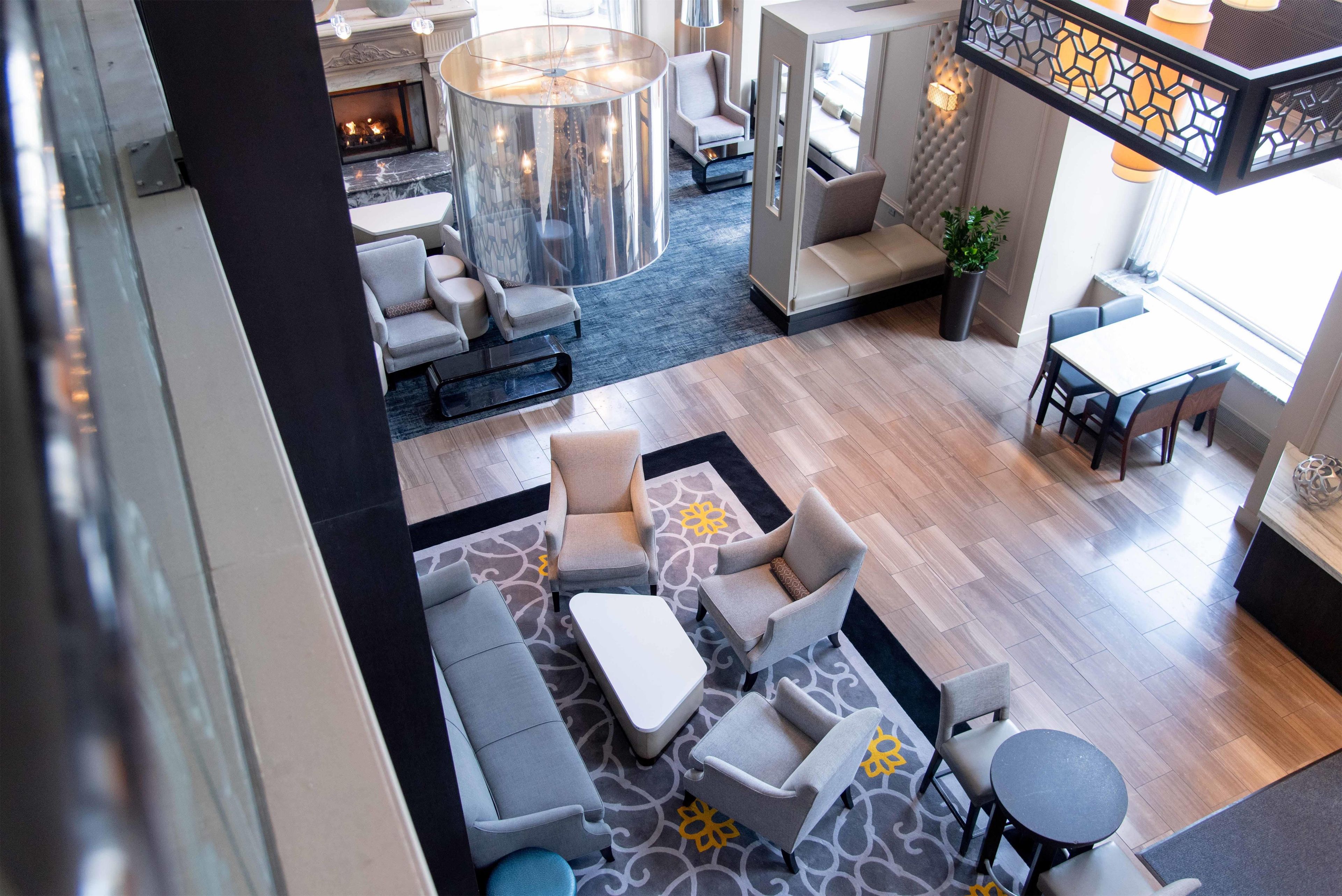 A hotel lobby with seating areas, a fireplace, and a staircase.