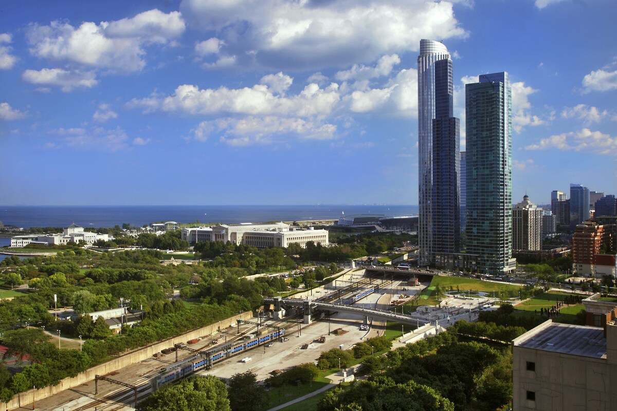 A cityscape with modern high-rise buildings, a train station, and a body of water in the background.