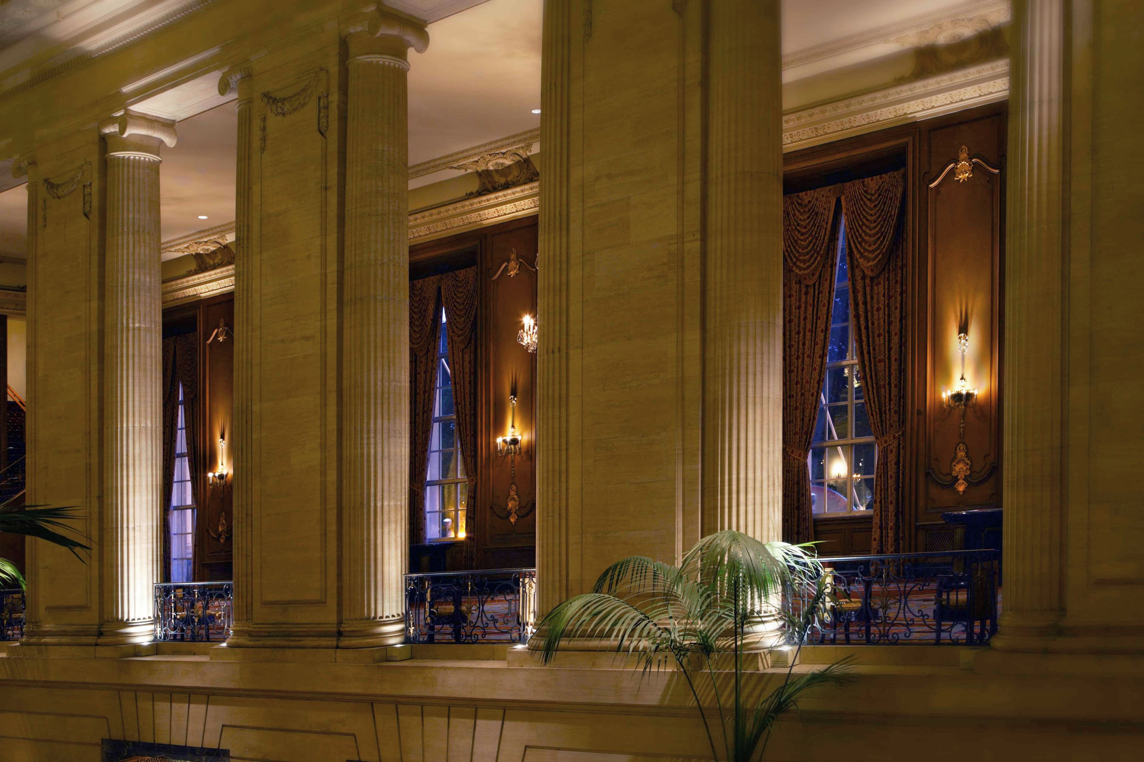 A grand lobby with classical columns, ornate chandeliers, and a large window with curtains.