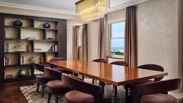 A dining area with a wooden table and six chairs, a bookshelf with various items, and a view through a window.