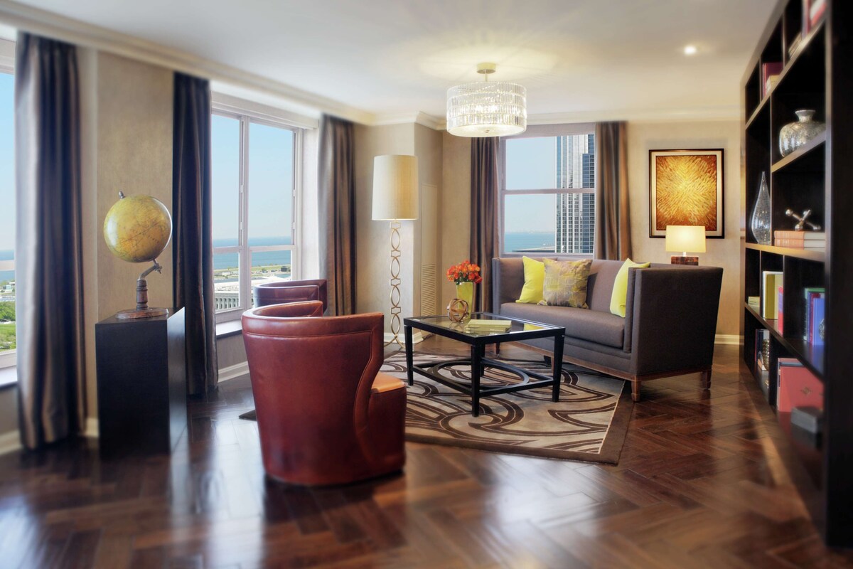 A spacious living room with a large window, a globe, a sofa, and a bookshelf.