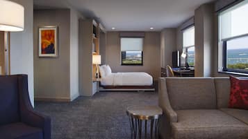 A hotel room with a bed, a sofa, a small table, a desk, and a large window with a view.