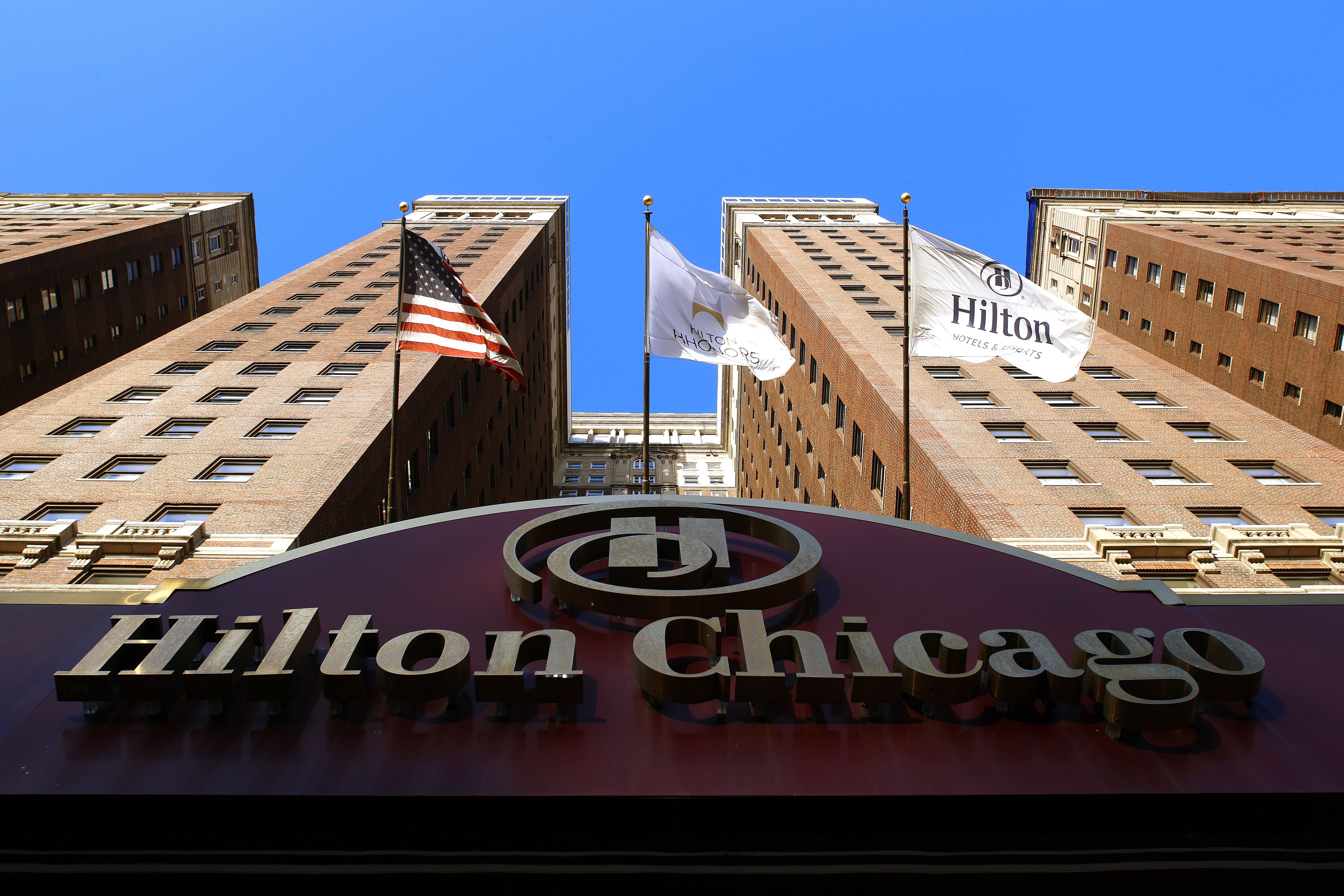 Il cartello dell'hotel Hilton Chicago con due bandiere, una americana e una del marchio Hilton, sullo sfondo di un cielo azzurro.