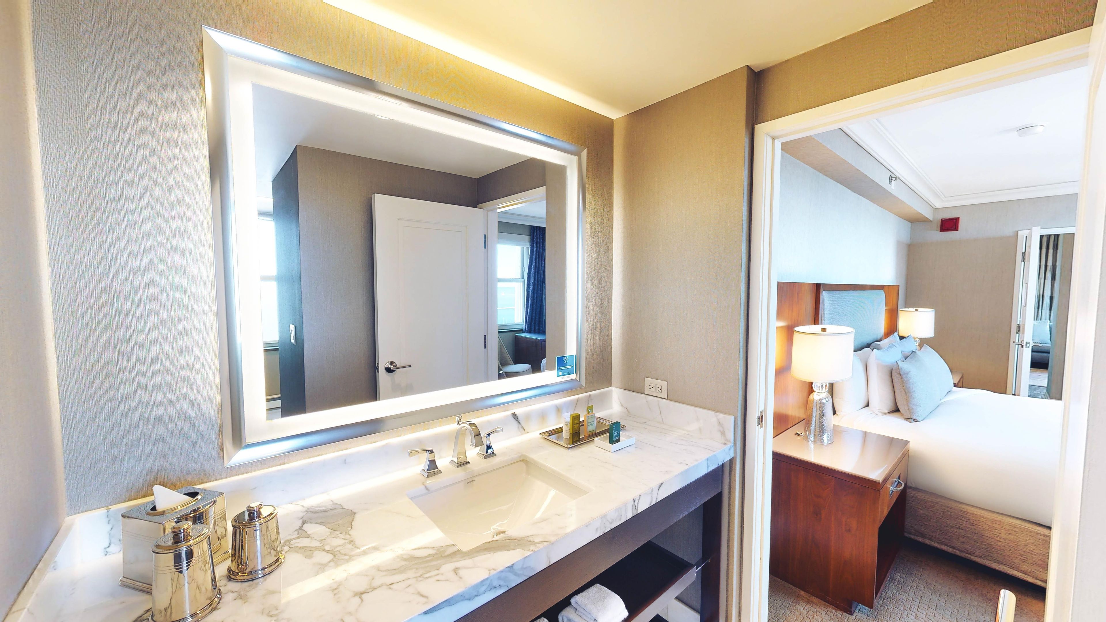 A hotel bathroom with a large mirror, a marble sink, and a wooden vanity.