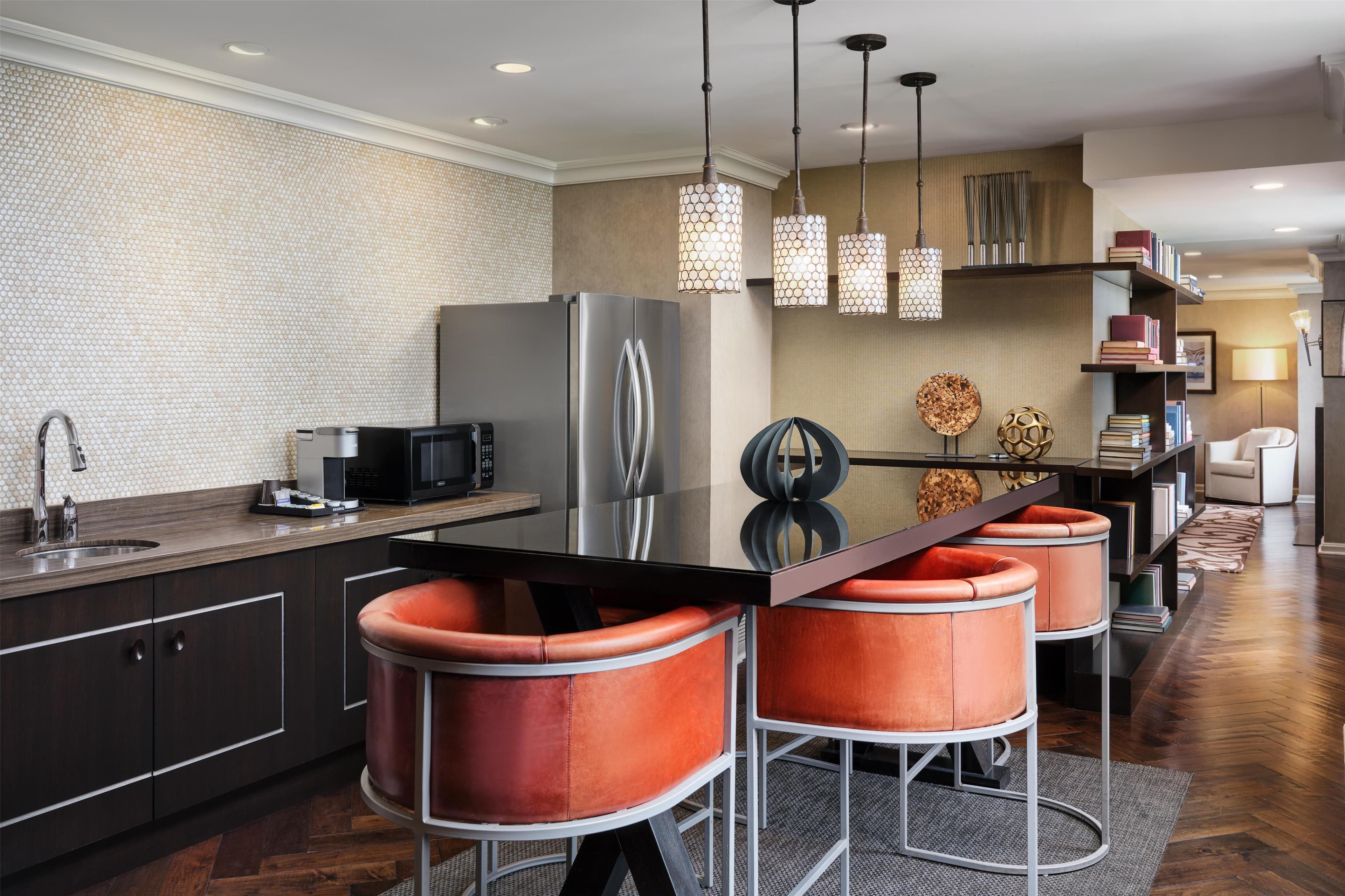 A modern kitchen with a large island, stainless steel appliances, and orange bar stools.